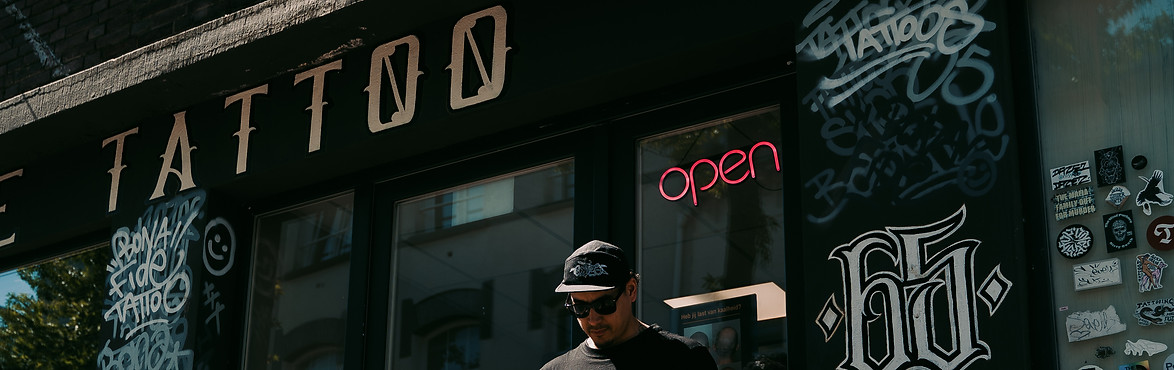 Ivan, tattoo artist at Bona Fide Tattoo in Heerlen, standing outside the black shop facade with large TATTOO letters