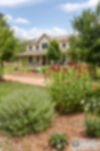 Large two-story house with gardens and red flowers.