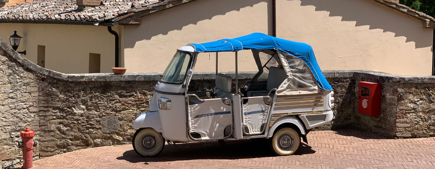 White three-wheeled vehicle with blue awning parked near building