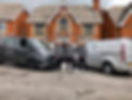 Three people in grey uniforms standing between two company vans in front of a house
