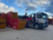 Side view of a truck loading a skip in the yard