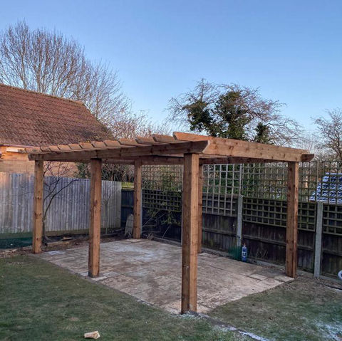 A wooden pergola over a patio with trellises in a backyard