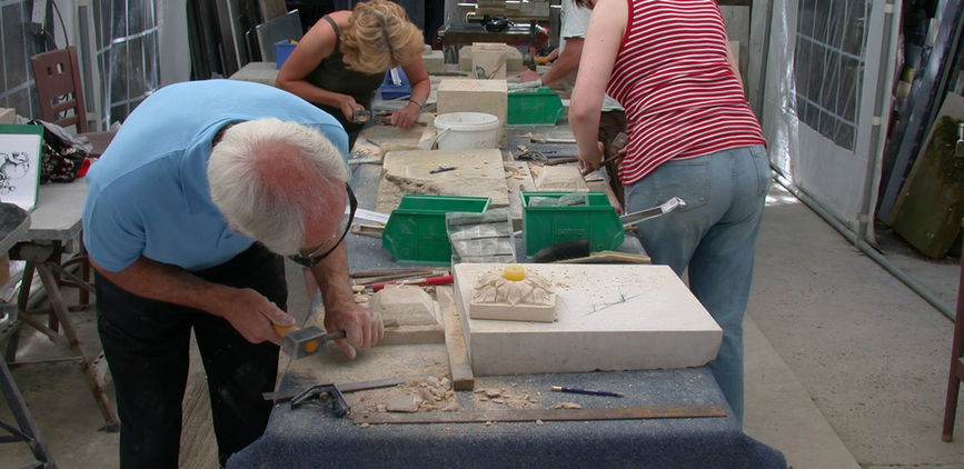 Three people carving stone sculptures on tables 