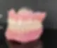 A realistic dental prosthesis showing upper and lower teeth with a pink synthetic base