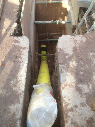 Looking down into a concrete trench at a yellow gas pipe being installed