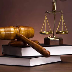 A wooden gavel rests on stacked legal books beside a golden scale of justice