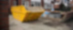 A yellow construction skip filled with debris on a residential driveway