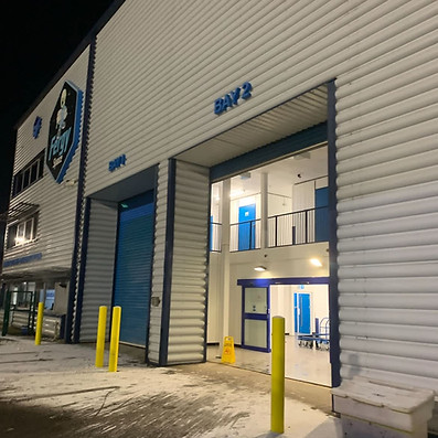 External loading bay of a storage facility building with safety bollards and a large open roller shutter door