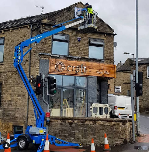 A technician in a blue lift stands elevated above six parked white vans with a group of uniformed workers below