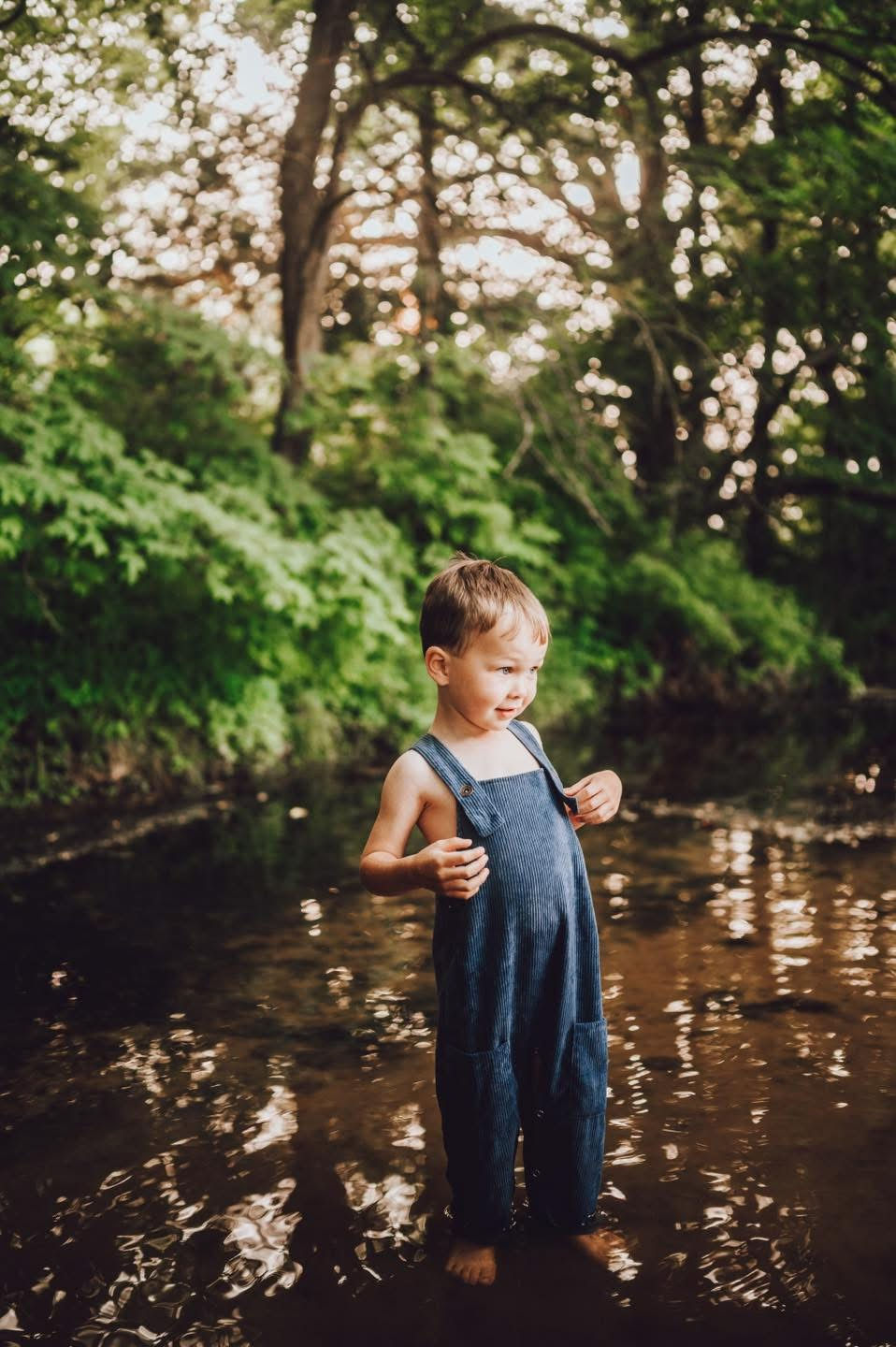 Young boy in overalls plays in a creek during creek photoshoot in Lexington Indiana
