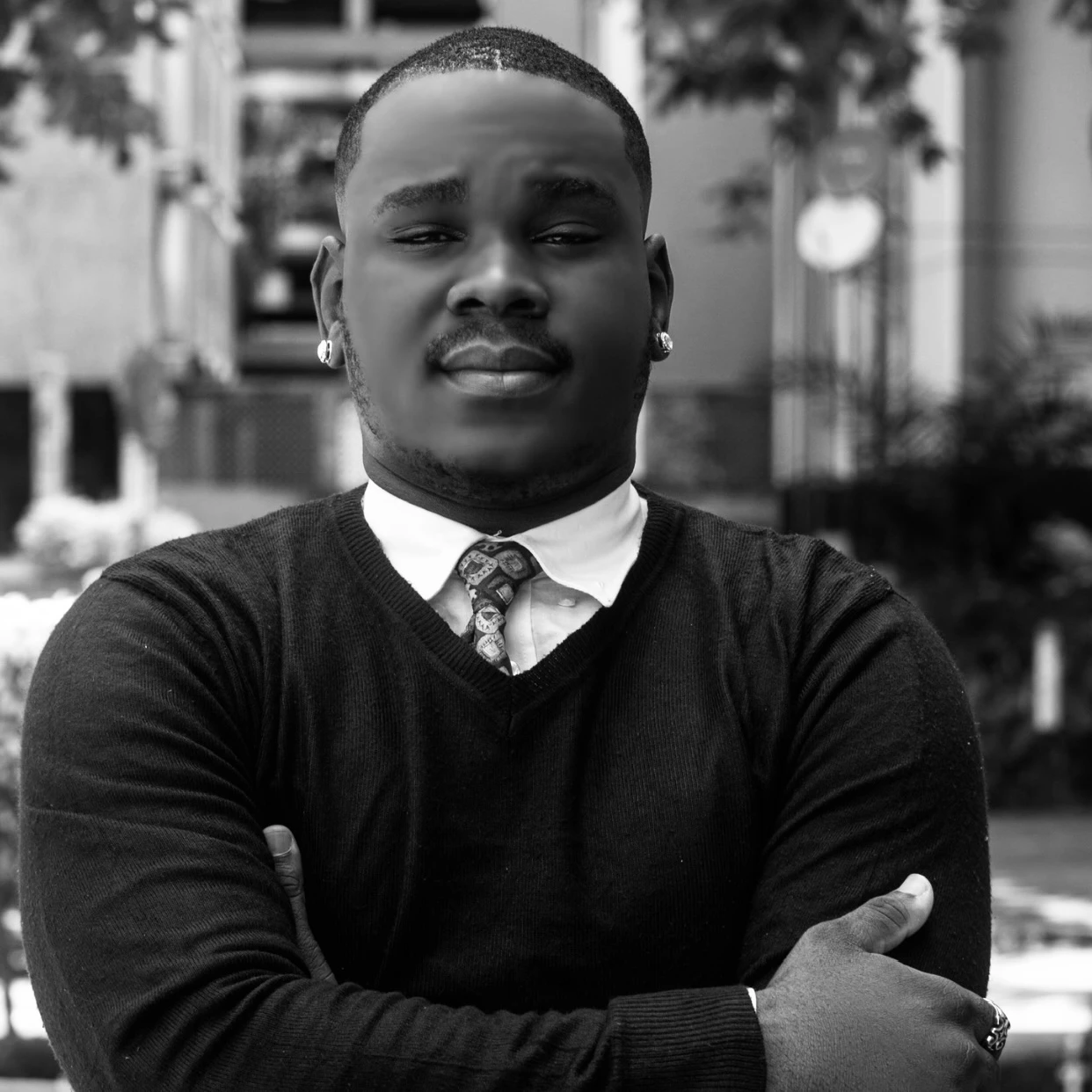A handsome young black man wearing a sweater, shirt and tie.