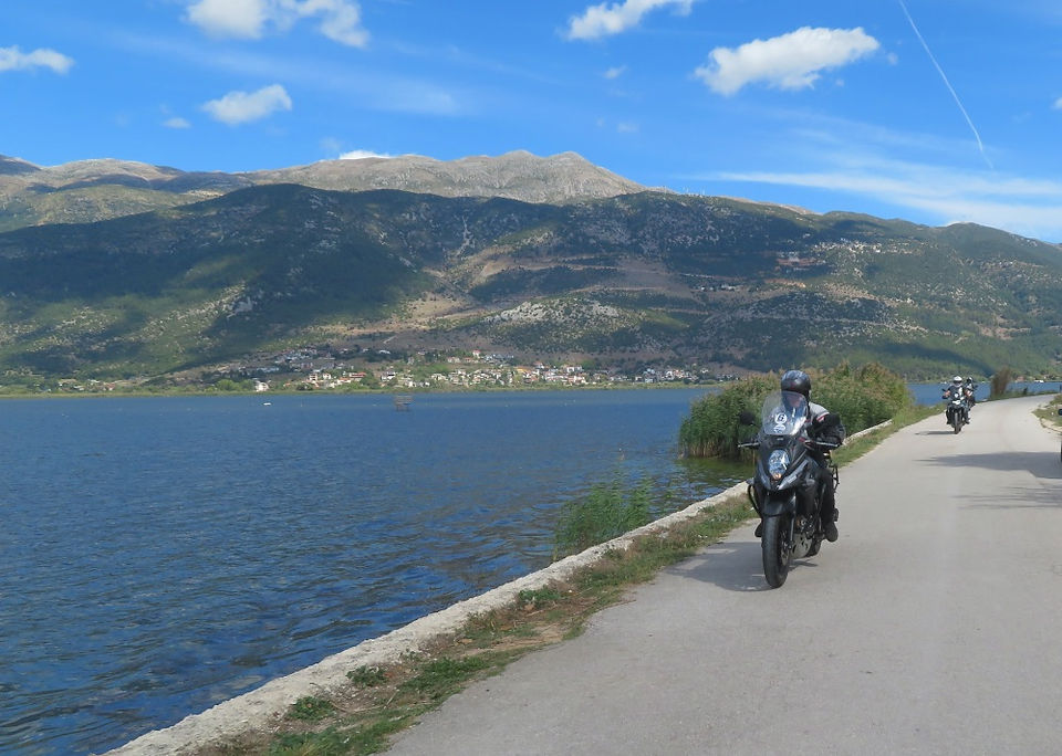 two bikers riding motorcycles near the sea doing a motorcycle tour in greece with Peterpanplanet, mountains in the background