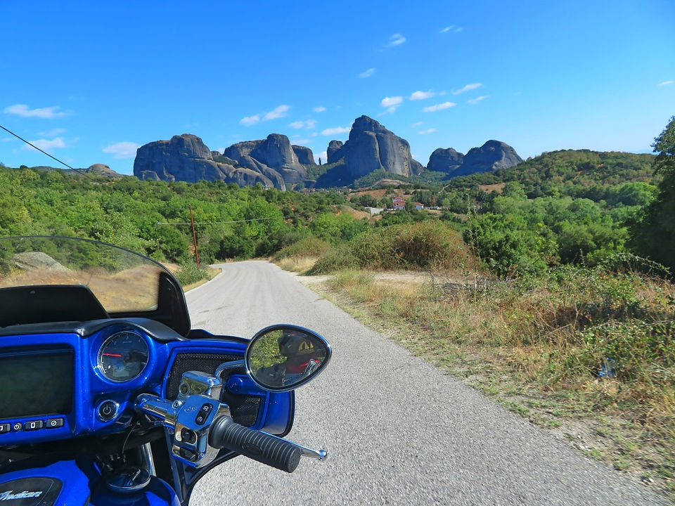 blue motorcycle riding in the green greek countryside and large rock mountains ahead