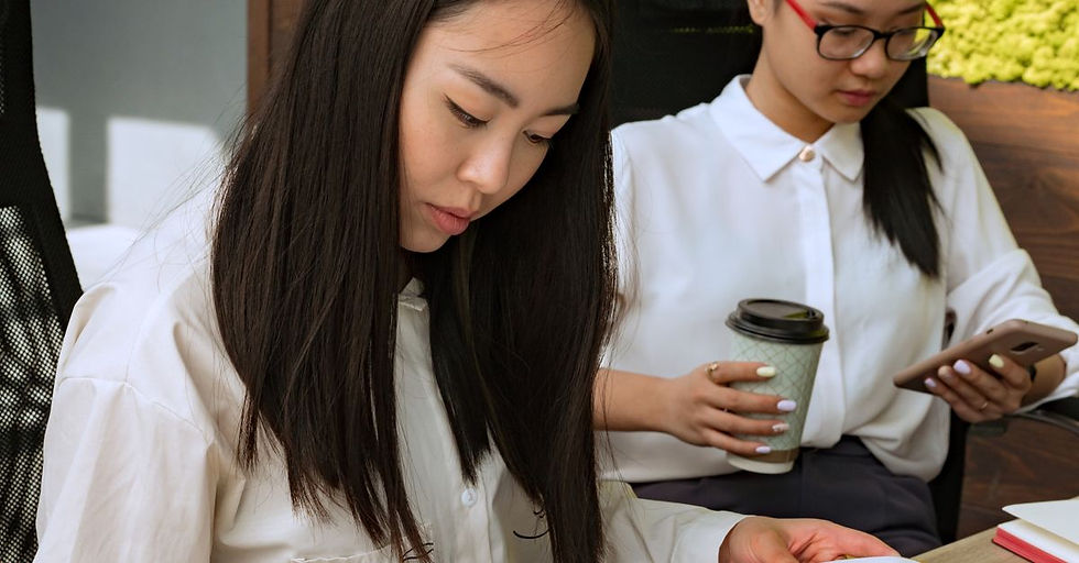 Two women focused on documents and a phone over coffee in a bright modern office