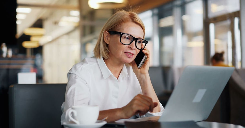 A mature professional woman works on a laptop and takes a call in a cafe.
