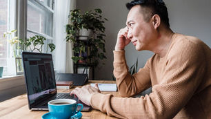 Asian man working on laptop at home desk with coffee and plants, side profile