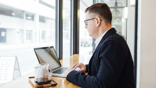 A man works on a laptop by a cafe window, focused and still in the search