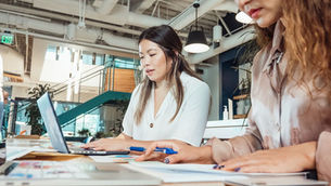 Two professionals focused on a laptop in a bright modern office, reviewing work together