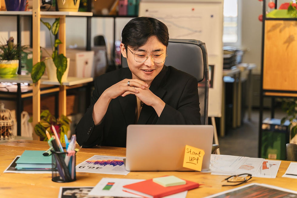 Asian professional smiling at his laptop in a bright office, working through his job search