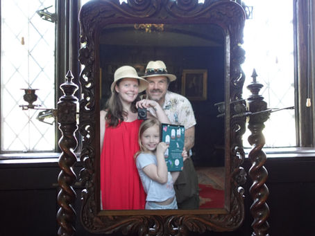 Smiling family of three in an ornate mirror selfie inside a historic room with leaded windows.