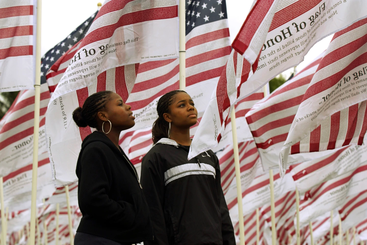 FILE - Identical twins Janita Ollison, left, and Jeannetta Ollison, 17, of Gresham, Oregon, try to read some of the names of 9/11 victims printed on more than twenty -six hundred "Flags of Honor" erected as a memorial to represent each person killed by terrorist attacks, Sept. 11, 2001, in Gresham Ore., Wednesday, Sept. 10, 2003. Americans are looking back on the horror and legacy of 9/11, gathering Monday, Sept. 11, 2023, at memorials, firehouses, city halls, and elsewhere to observe the 22nd anniversary of the deadliest terror attack on U.S. soil. (AP Photo/John Klicker, File)