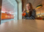 Woman smiling while sipping a drink at a table on a ferry. Background shows an orange lifeboat and ferry interiors with warm lighting. AvVida.co.uk - Adventure Motorcycle Travel