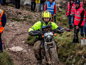 Female rider on restart of Blue Hills 2 on the 102nd Lands End Trial 2026. Rider wearing neon yellow helmet and jacket. Motorcycle Scorpa TY125 covered in mud.