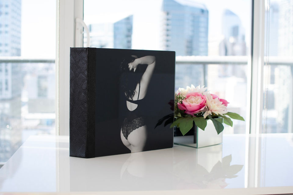 Boudoir book with black and white acrylic cover on a white table with pink flowers with downtown Calgary in the background.