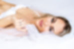blonde woman in white lingerie and wedding veil laying on a white bed and smiling for boudoir photoshoot.