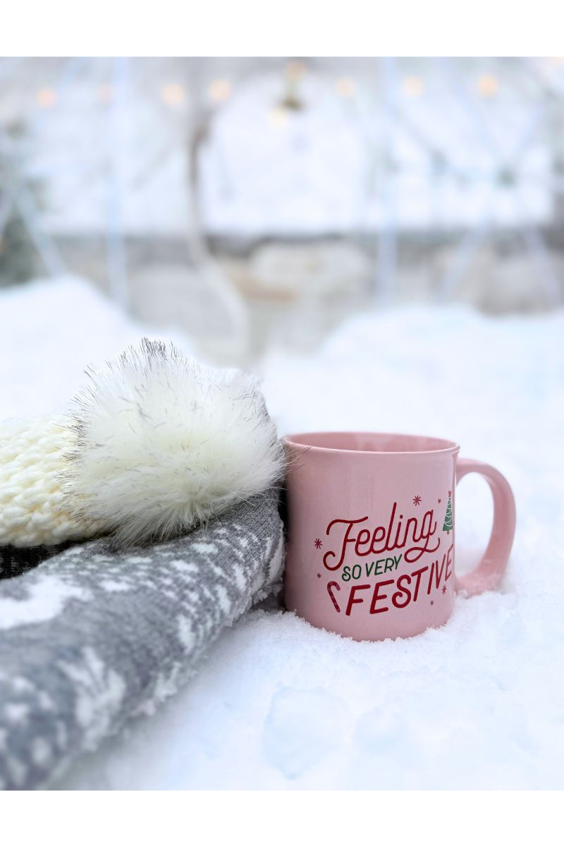 a cozy toque and fuzzy socks with a pink mug sitting in the snow with luxury winter igloo in the background
