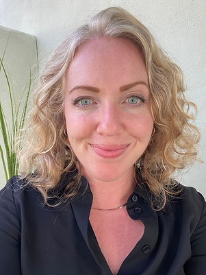 Headshot of reddish blonde curly haired fair skined woman in black collared blouse against light background.
