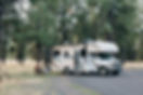 A couple sitting on camping chairs in front of an RV in the woods
