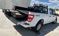 White 4x4 pickup truck with its tailgate lowered and a sliding cargo-bed tray extended, revealing organized storage compartments.