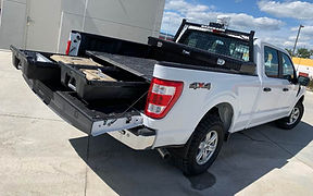 White 4x4 pickup truck with its tailgate lowered and a sliding cargo-bed tray extended, revealing organized storage compartments.