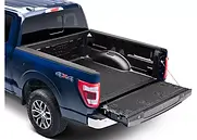 Black ribbed drop-in bed liner installed in a blue 4x4 pickup with the tailgate open.