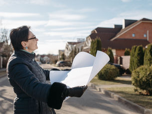 Woman holding architectural plans while looking at houses on a residential street