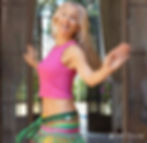 Tight shot ofbelly dancer Jensuya smiling at camera as she does a spin with colorful hip scarf and pink tank top.