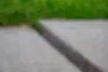 A close-up of misaligned concrete slabs with a gap in between, next to grass