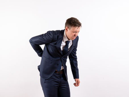 A man in a suit with his right hand on his lower back, indicating back pain.