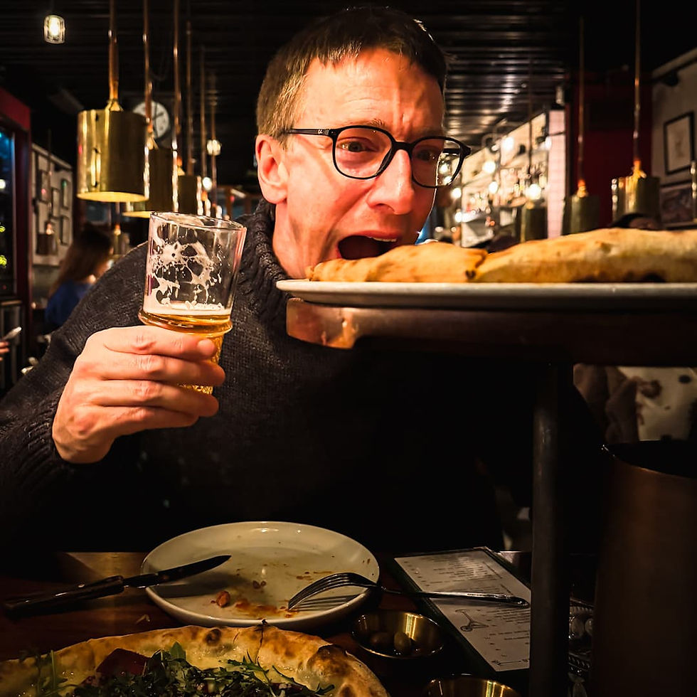 James holding his beer and trying to put his mouth around a pizza elevated on a pizza stand at Casa Inferno, one of the best restaurants in Tromso