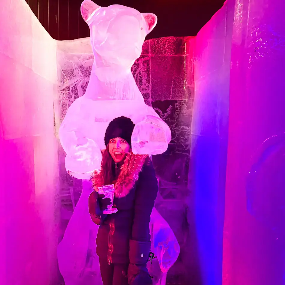 Shal holding an ice glass inside Magic Ice Bar in Tromsø, standing in front of illuminated ice bear sculpture with pink and purple lighting — fun indoor things to do in Tromso in winter.