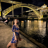 Shal standing in a cocktail dress with the steel bridge illuminated yellow behind her.