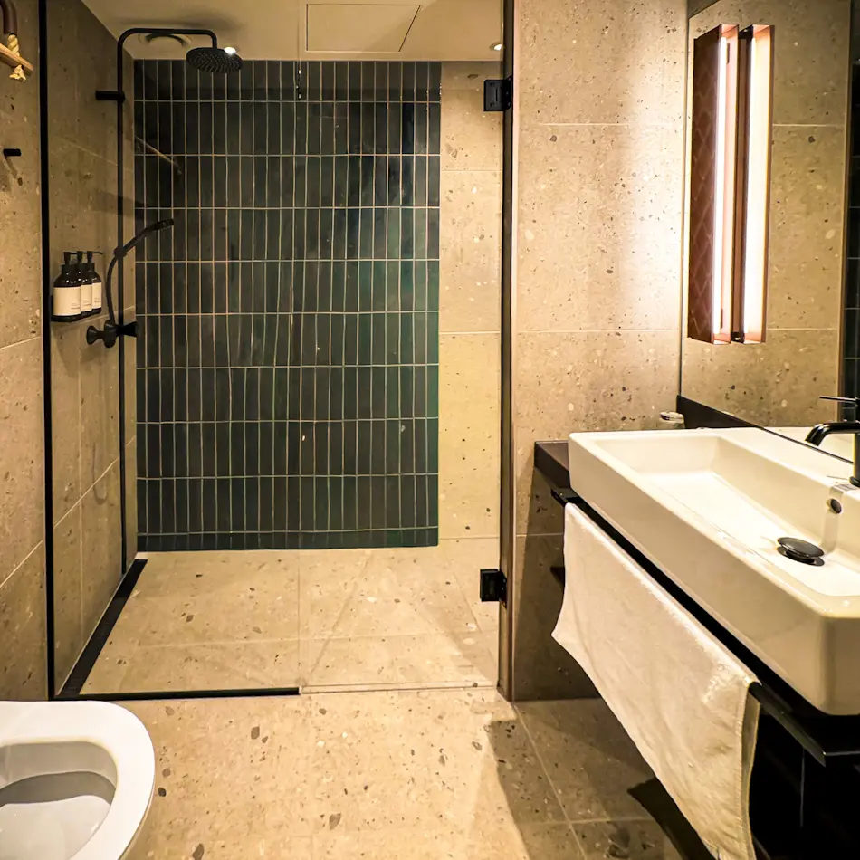 Modern bathroom at The Dock 69°39 by Scandic, one of the luxury hotels in Tromso, featuring a walk-in rainfall shower, tiled walls and minimalist sink design.