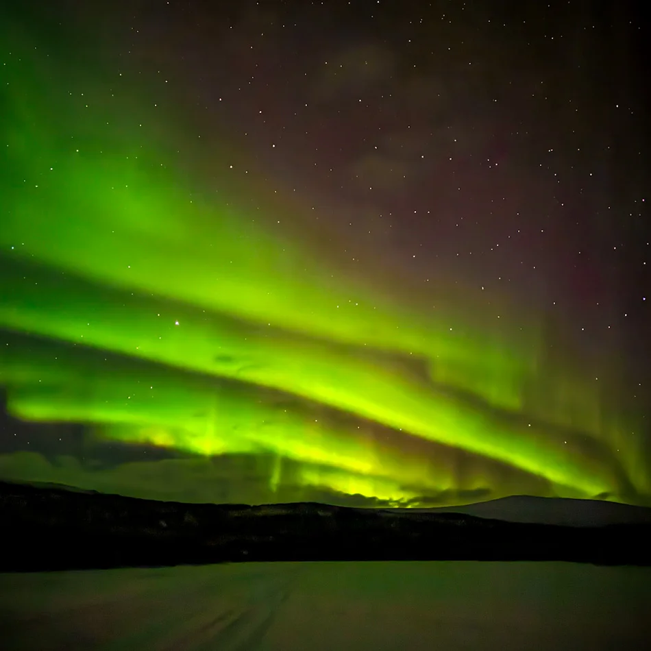 Bright green northern lights dancing over snowy landscape in Finland on our Tromso itinerary