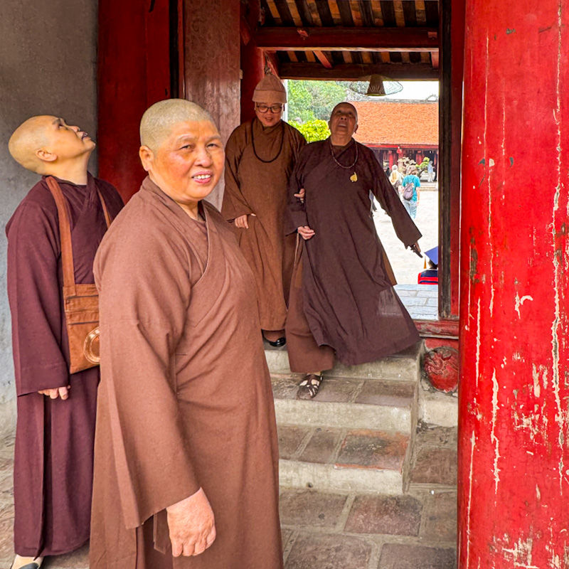 Buddhist monks in brown robes standing in a red doorway at Hanoi’s Temple of Literature, capturing a quiet everyday moment on our Vietnam 3 week itinerary through the cultural heart of the capital.