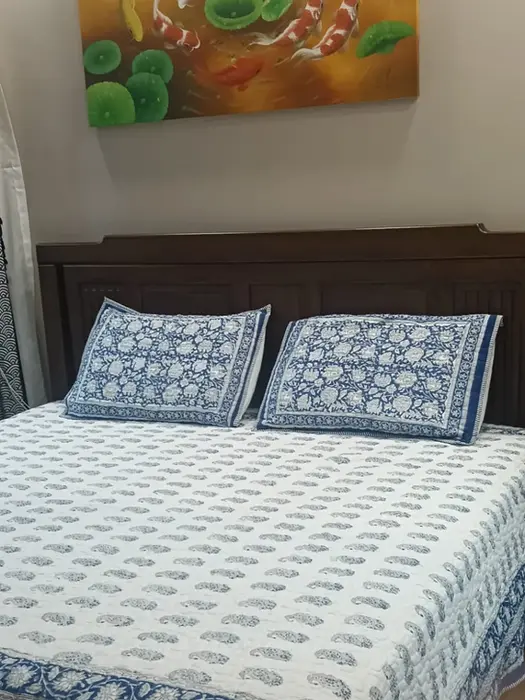 Bed with blue and white patterned sheets, wooden headboard, lotus painting.