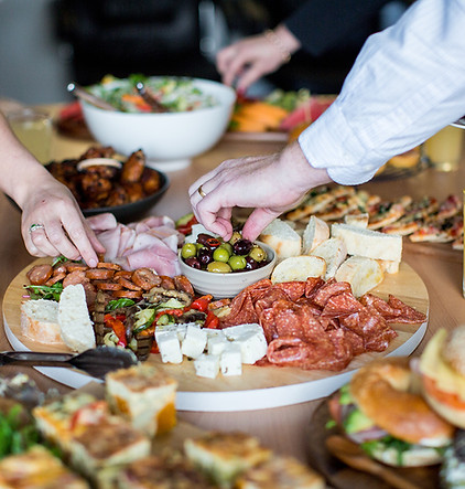 Hands reaching for food on a table piled high with catering options