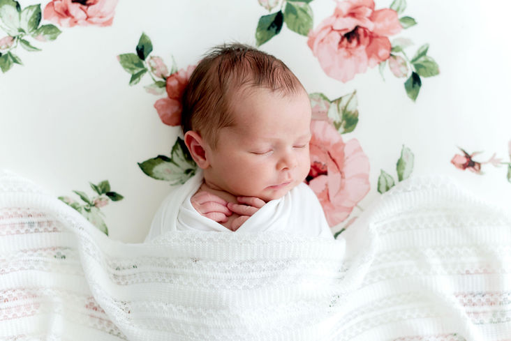 Photo d'un petit bébé nouveau-né fille qui dort sur le dos sur un fond fleuri dans les tons roses et blancs