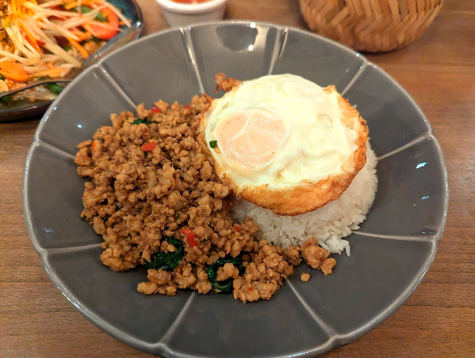Spicy minced pork with, small parts of red chilli and Thai basil, next to a mound of white rice and topped with a white fried egg.
