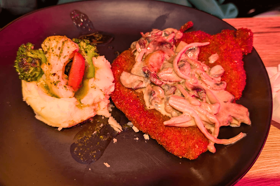 Crispy chicken schnitzel served with creamy mushroom sauce, mash, and vegetables.